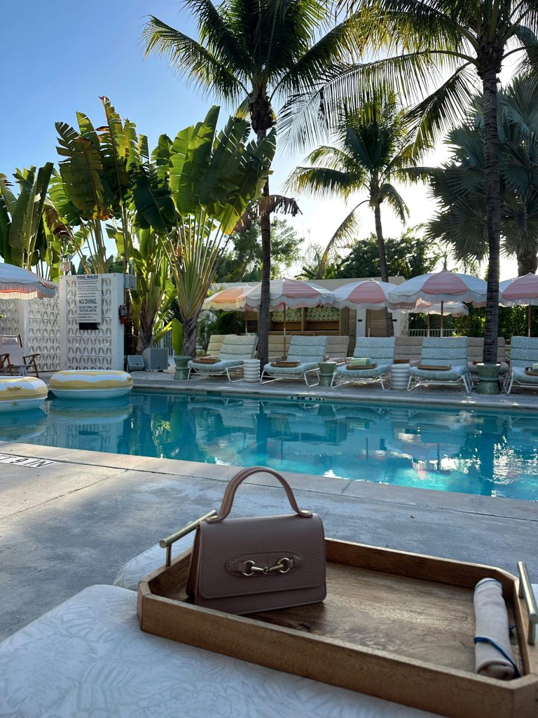Chic poolside scene with palm trees, umbrellas, and a stylish handbag.