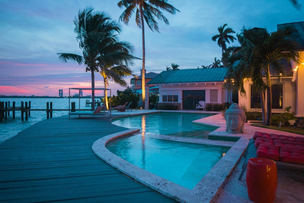 Experience a serene tropical villa with a poolside view during sunset in Miami Beach, featuring palm trees and tranquil waters.